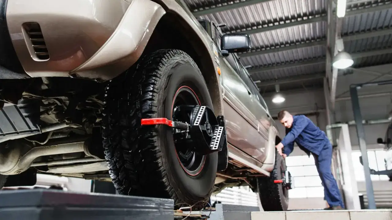 Mechanik sprawdza zbieżność kół w samochodzie terenowym na podnośniku.