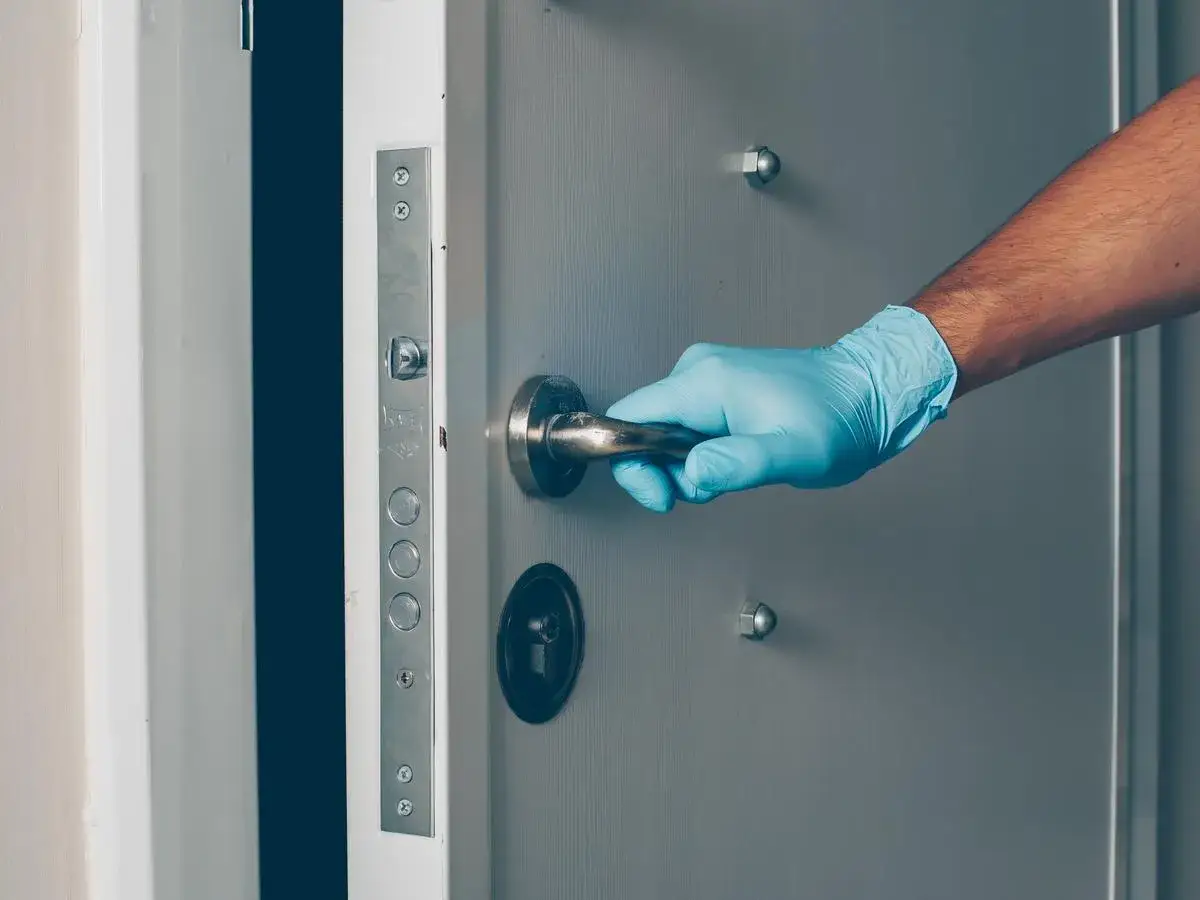 Main gantée bleue tente d'ouvrir une porte blindée, suggérant une tentative d'effraction.