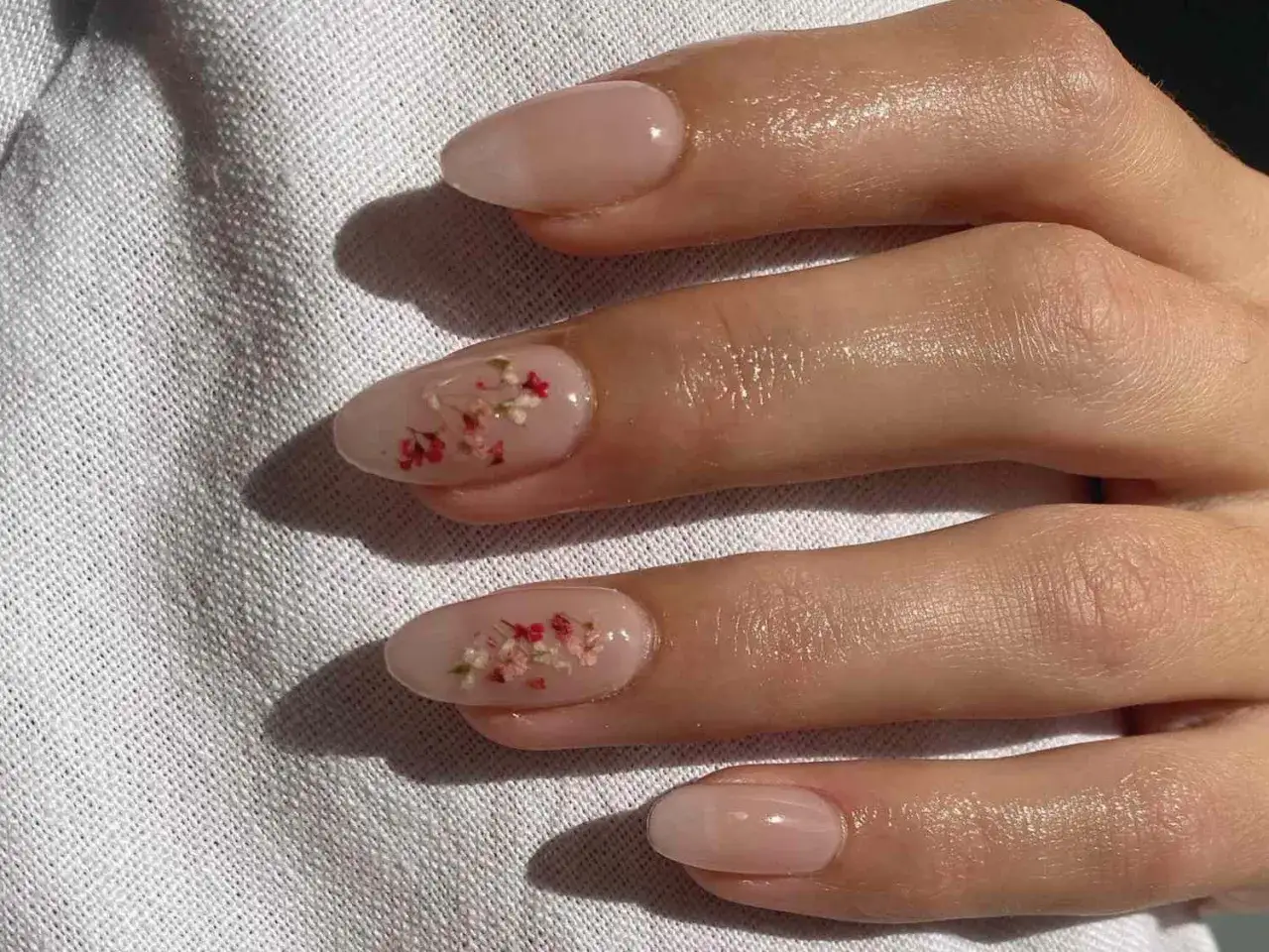 Vackra naglar med blommor i en naturlig, ljusrosa nyans. Sm&aring;, torkade blommor &auml;r inb&auml;ddade i nagellacket f&ouml;r en unik och delikat look.