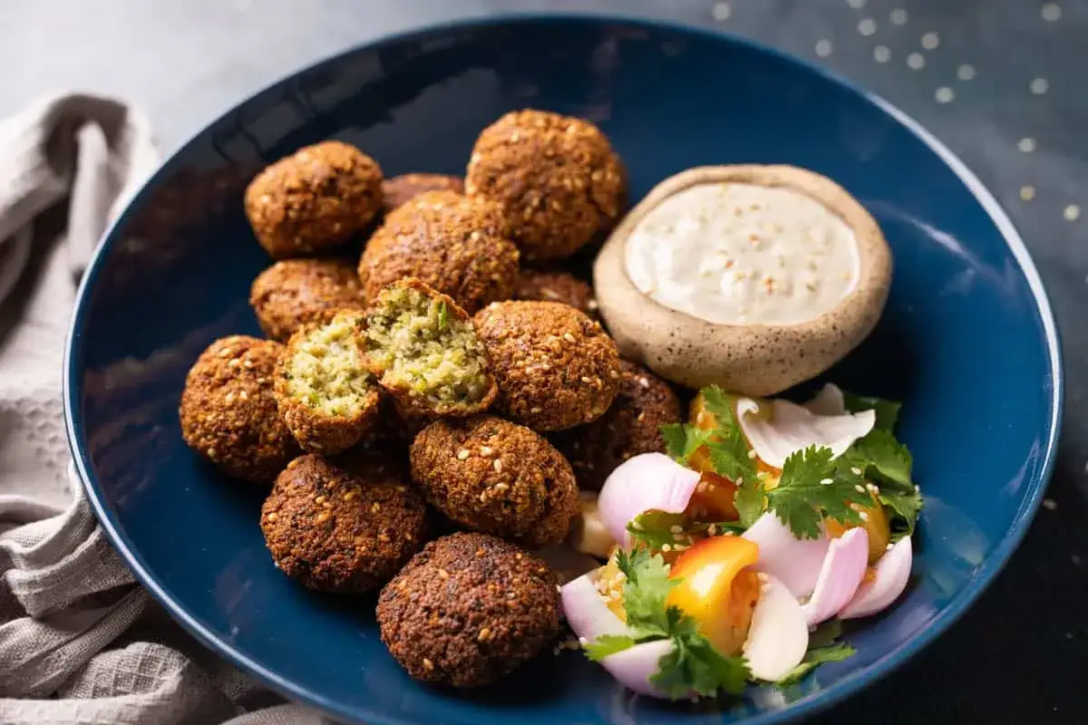 Ein Teller mit knusprigen Falafel, Tahini-Dip und frischem Salat. Perfekt für ein leckeres Falafel Rezept.