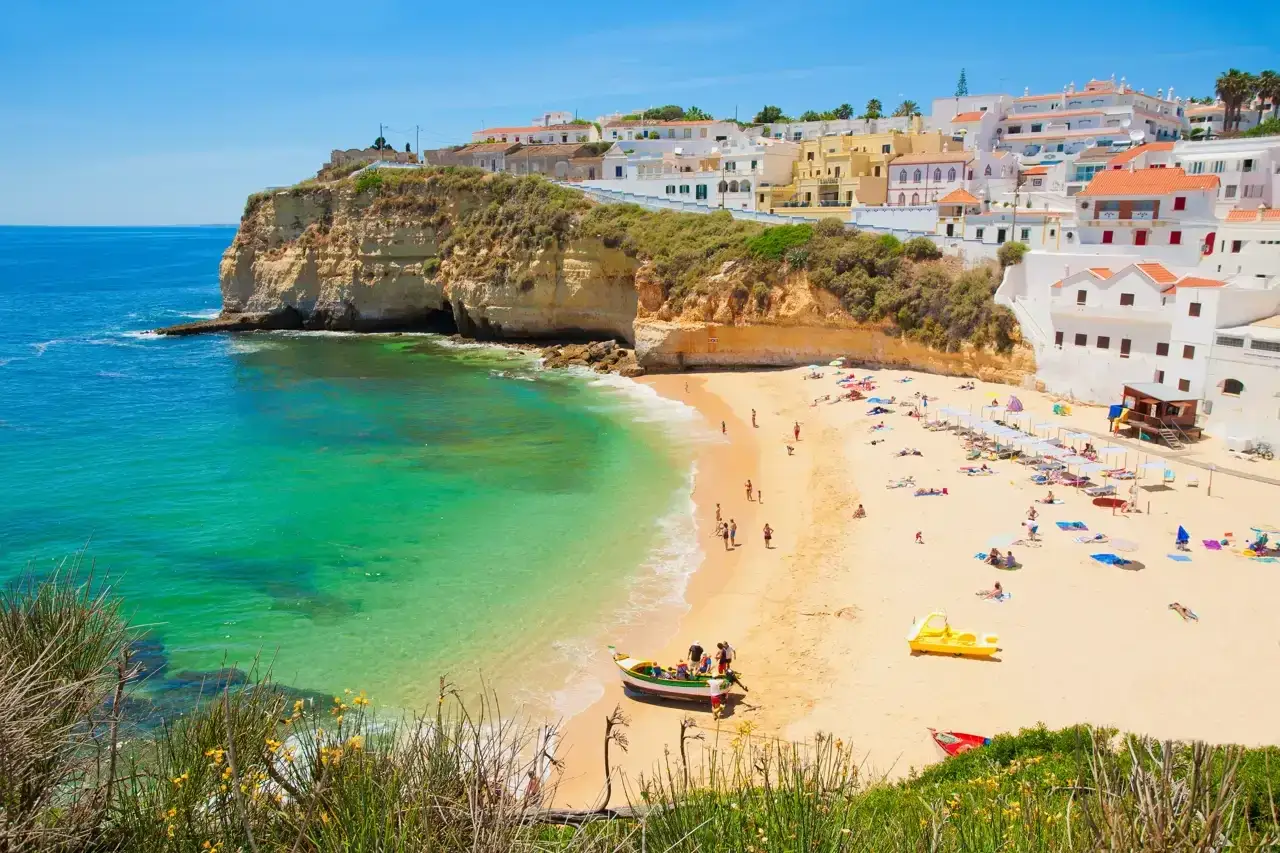 Hermosa playa de lagos con aguas turquesas, arena dorada y casas blancas en la colina. Gente disfrutando del sol y el mar.