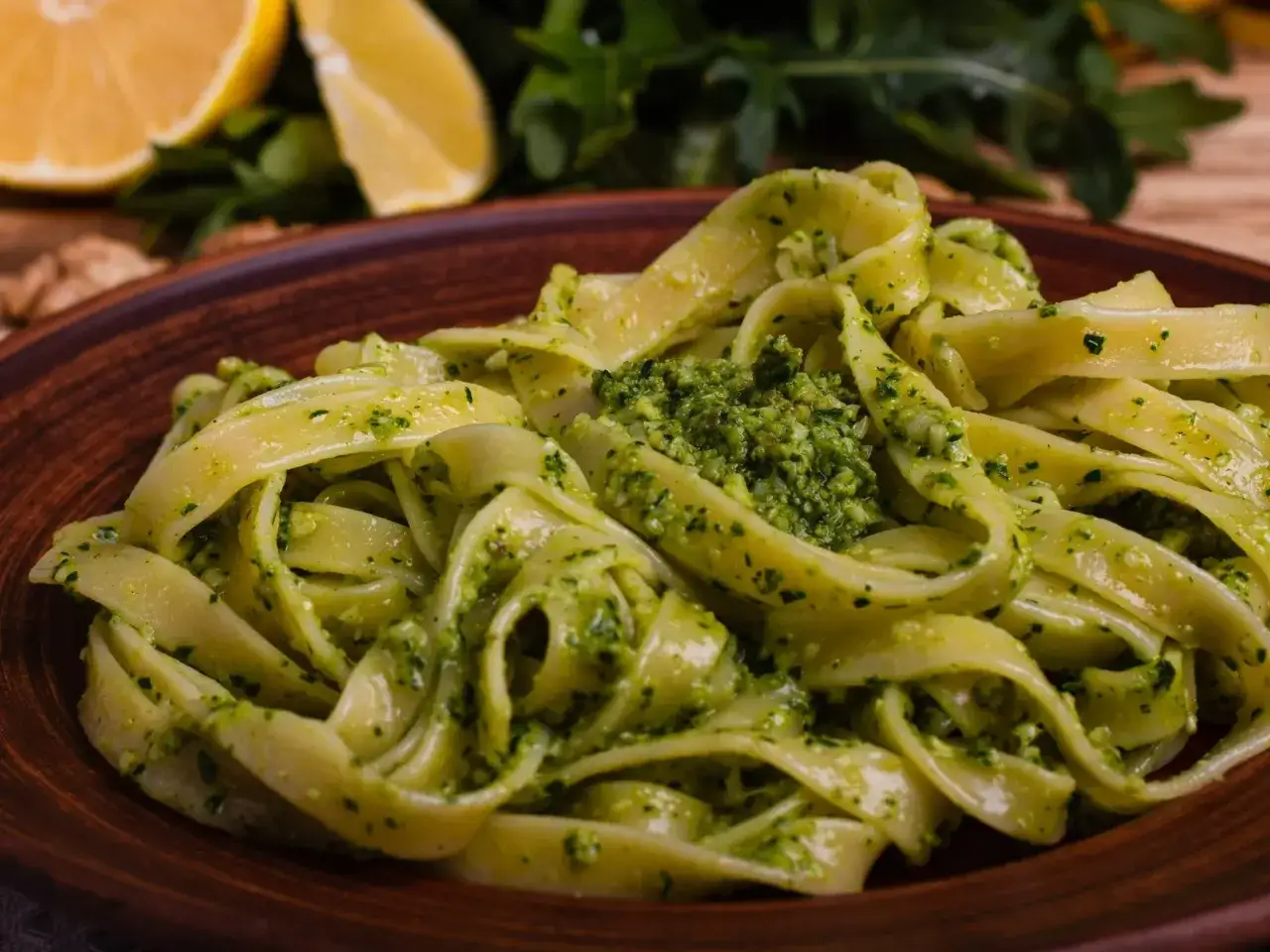 Pyszne, świeże pesto z makaronem, podane na glinianym talerzu. W tle cytryny i rukola.