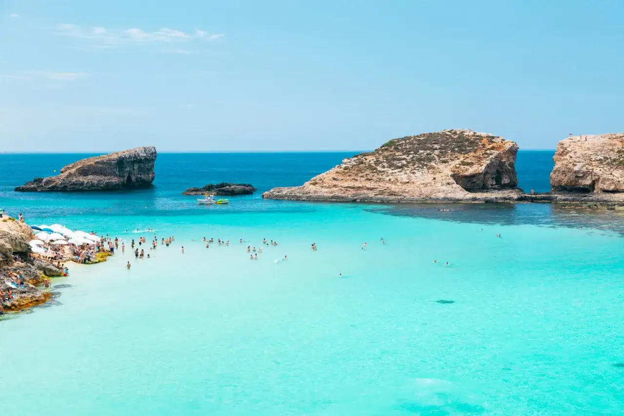 Malta: turkusowa woda, skaliste wybrzeże i tłumy ludzi cieszących się słońcem na plażach.