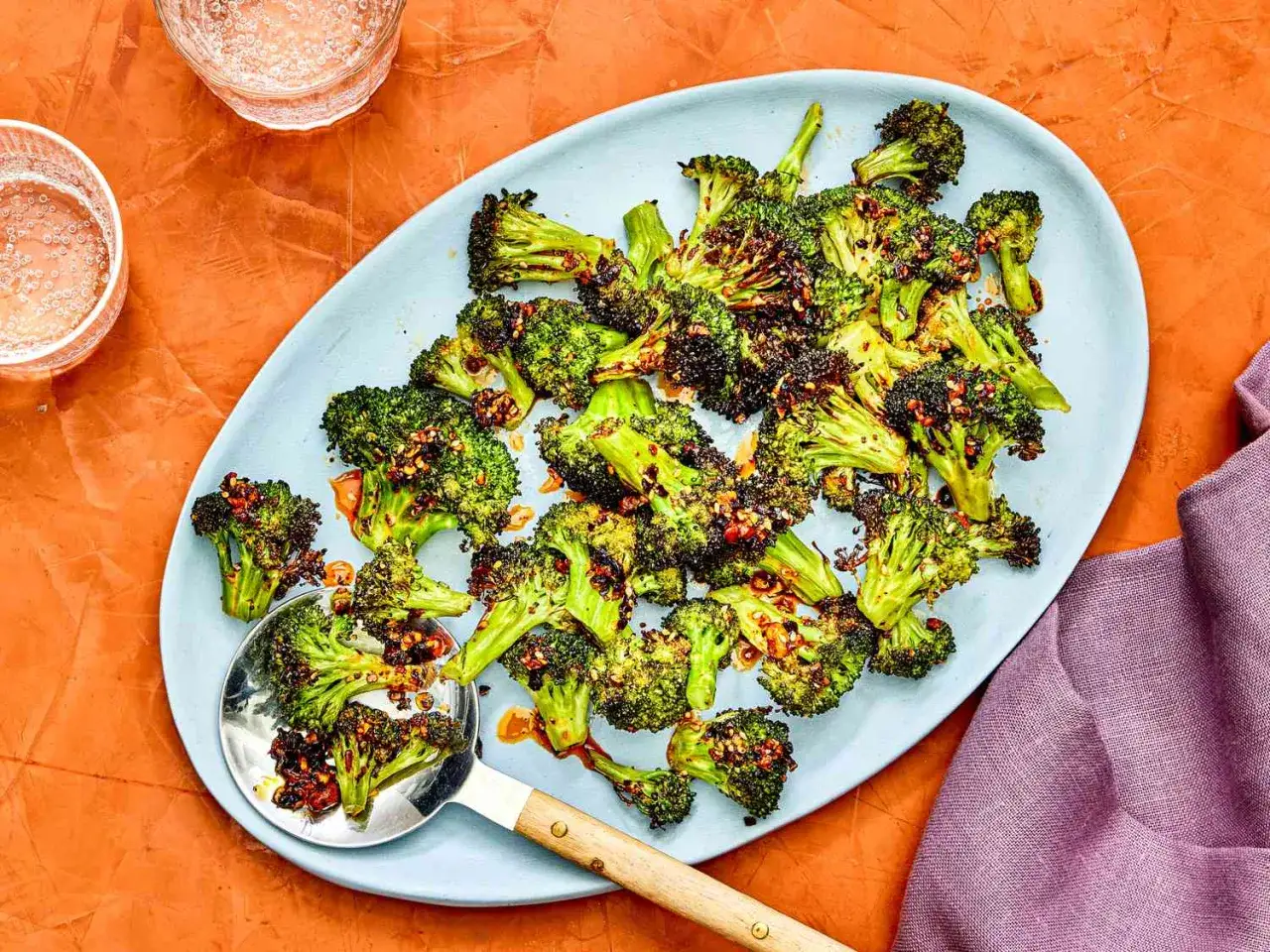 Brocoli en airfryer, crujiente y dorado, servido en una bandeja azul con un aderezo brillante.