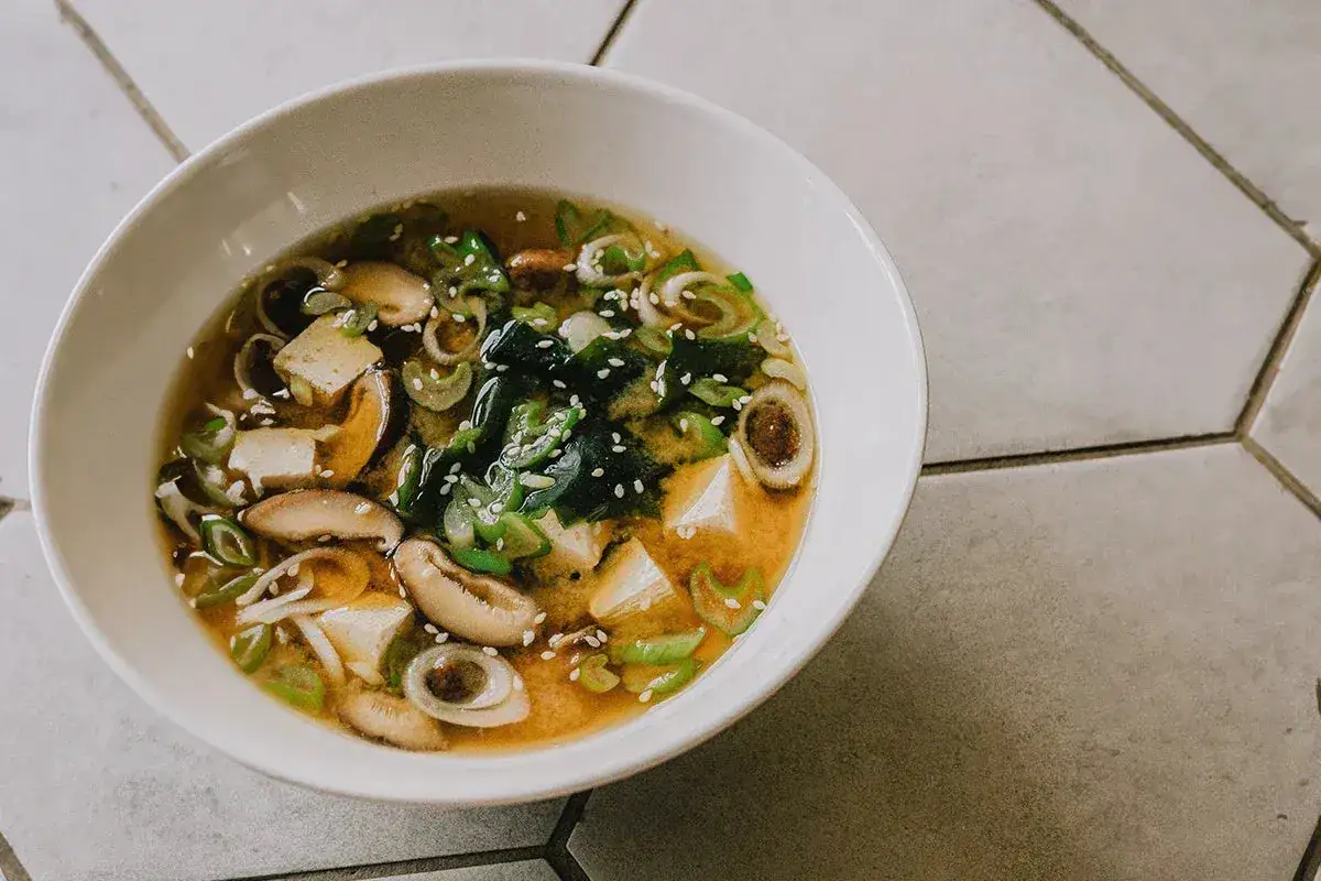 A miska pełna aromatycznej zupy miso z kostkami tofu, grzybami shiitake, wodorostami wakame i szczypiorkiem, posypana sezamem.