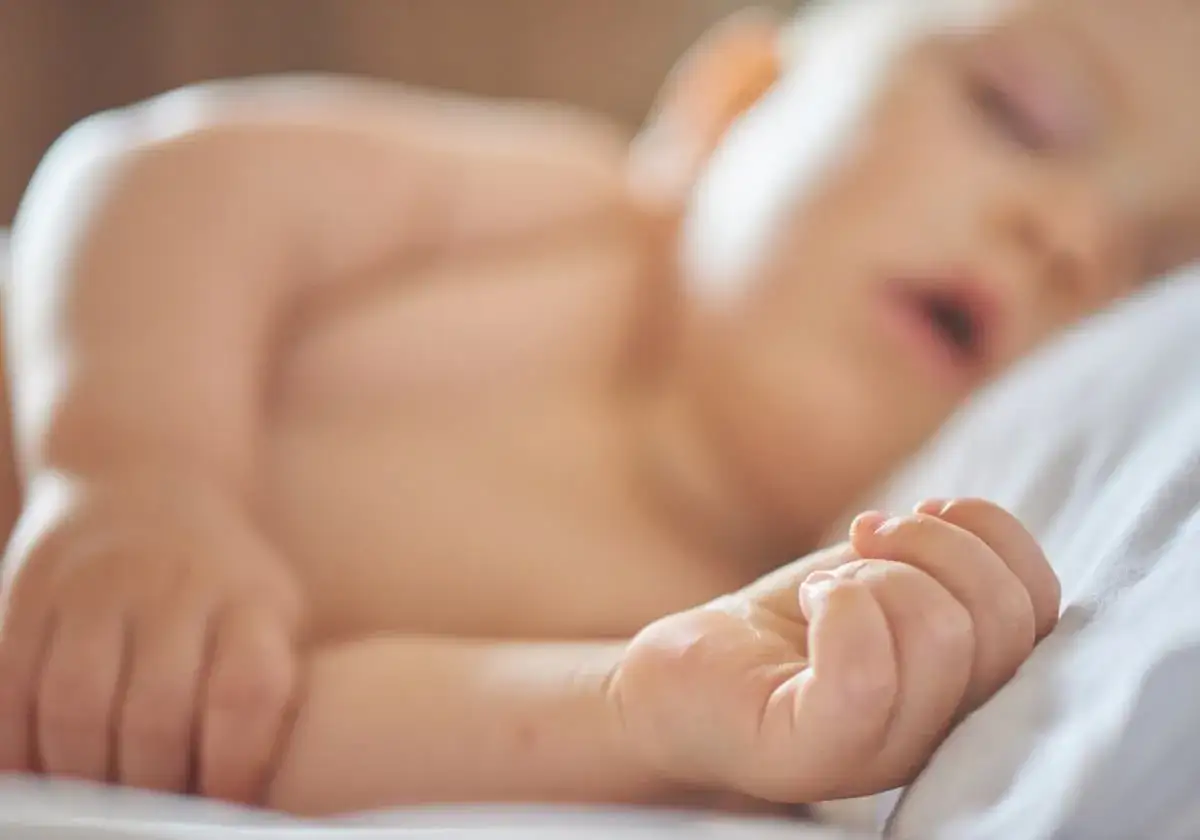 En 5 m&aring;naders bebis sover djupt, men kanske vaknar ofta p&aring; natten. Liten hand vilar p&aring; kudden.