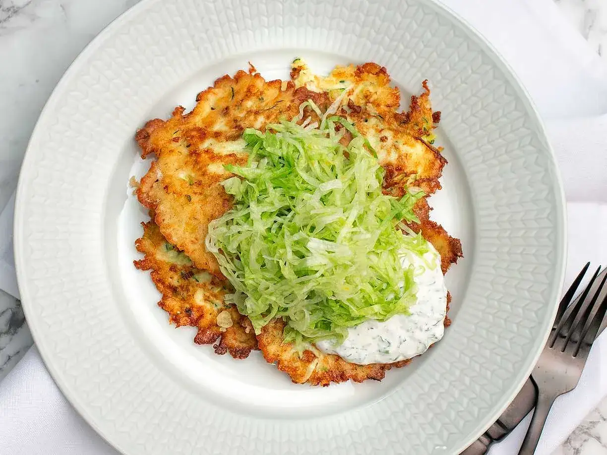 Krispiga plättar med riven zucchini, toppade med färsk sallad och en klick krämig sås. Ett perfekt zucchini recept för en lätt lunch.