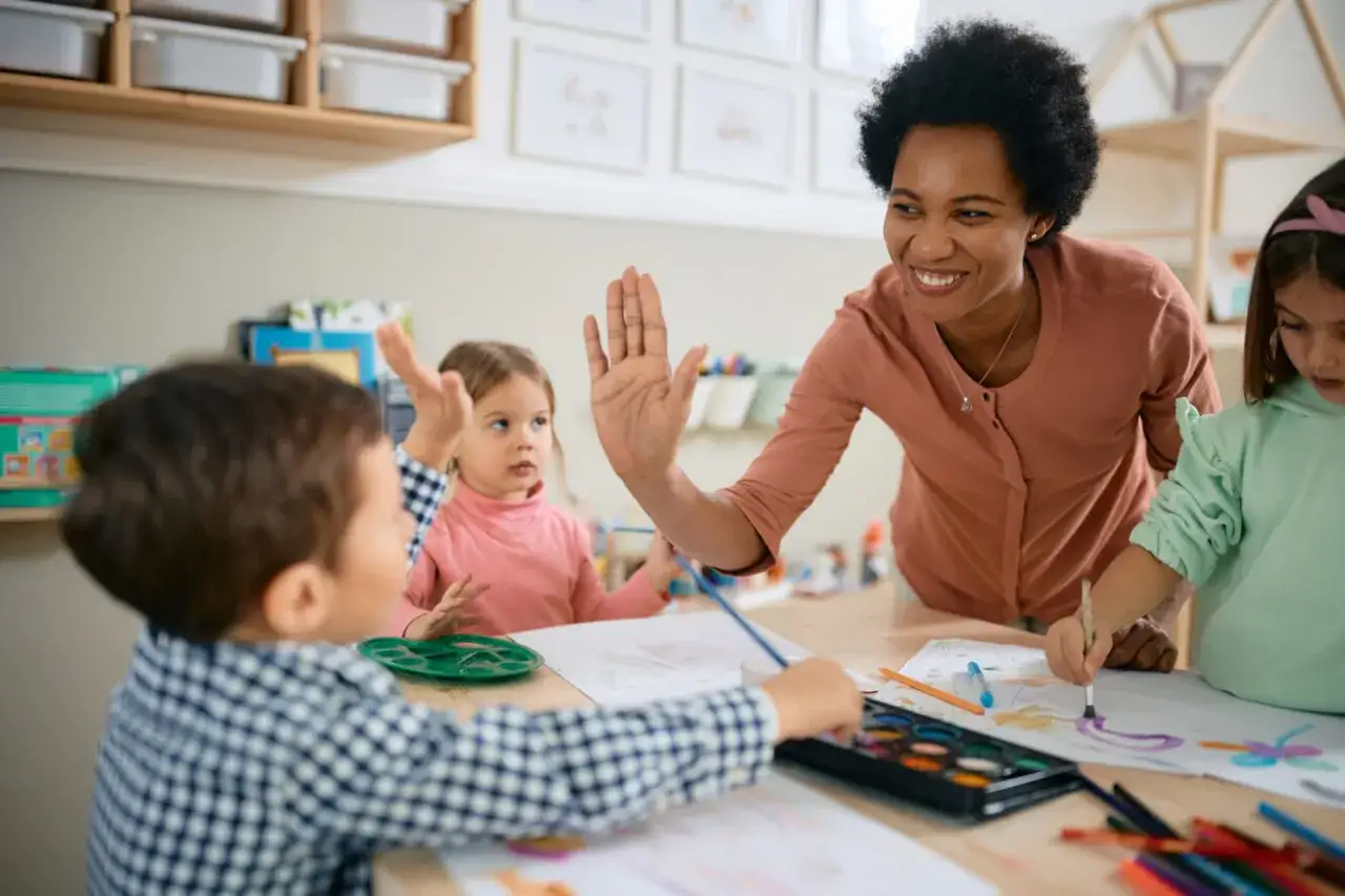 Lehrerin gibt High-Five f&uuml;r Achtsamkeit im Unterricht. Kinder malen konzentriert.