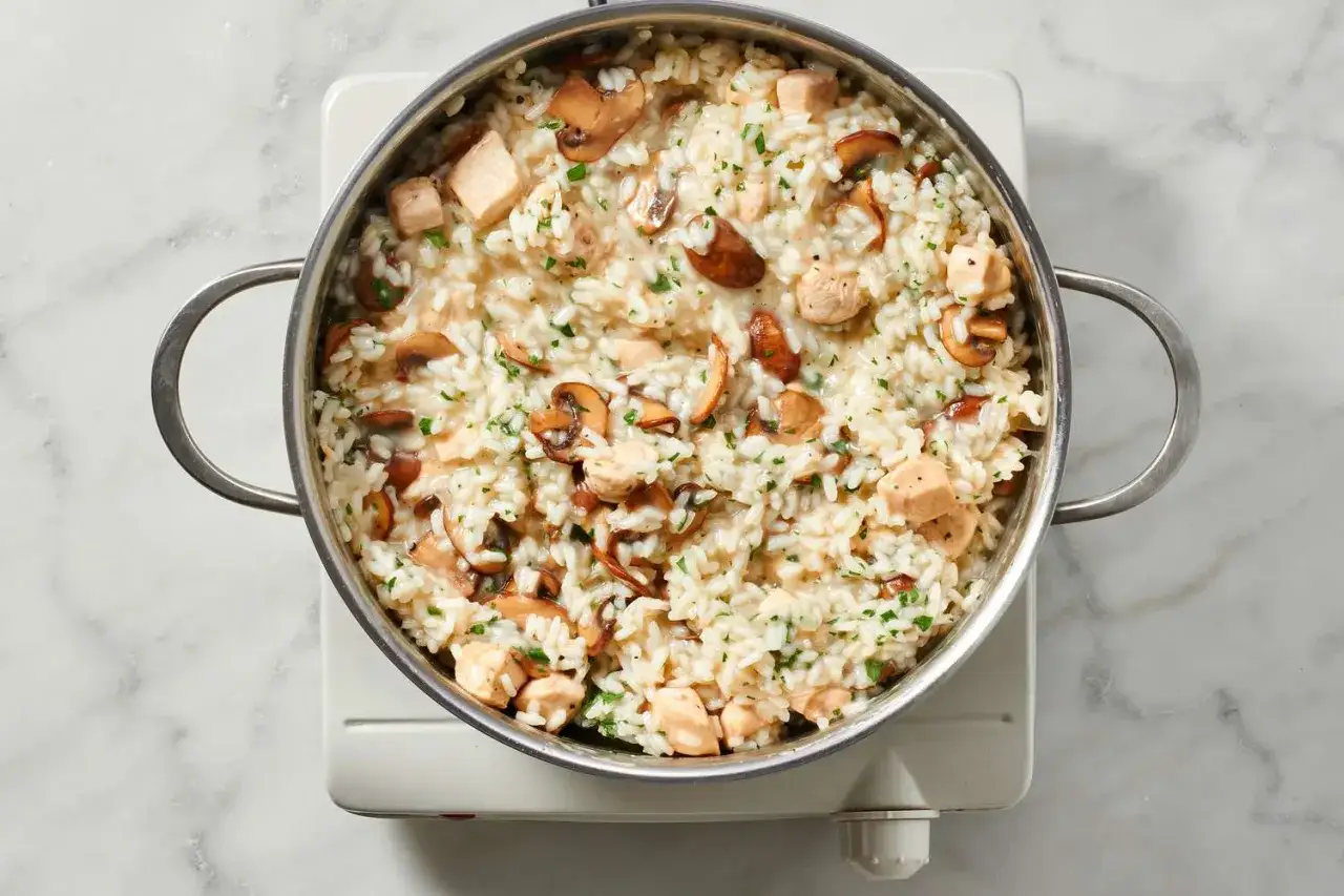 Un crémeux risotto poulet champignon, garni de persil frais, dans une casserole en acier inoxydable.