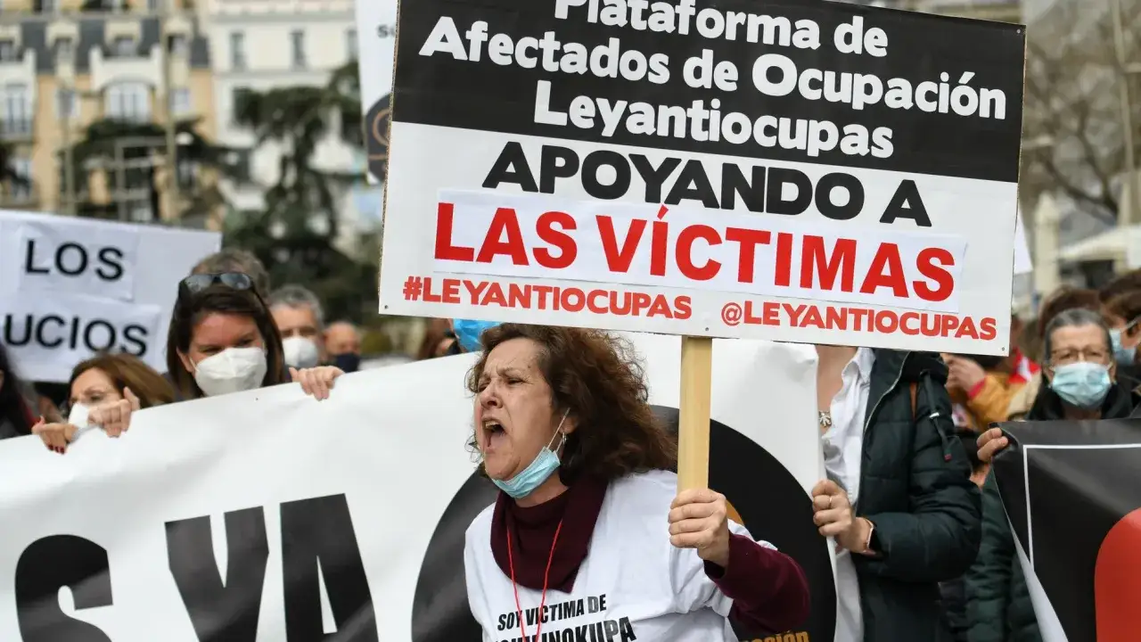 Manifestantes en Espa&ntilde;a protestan contra los okupas, apoyando a las v&iacute;ctimas. Una mujer grita con un cartel que dice 