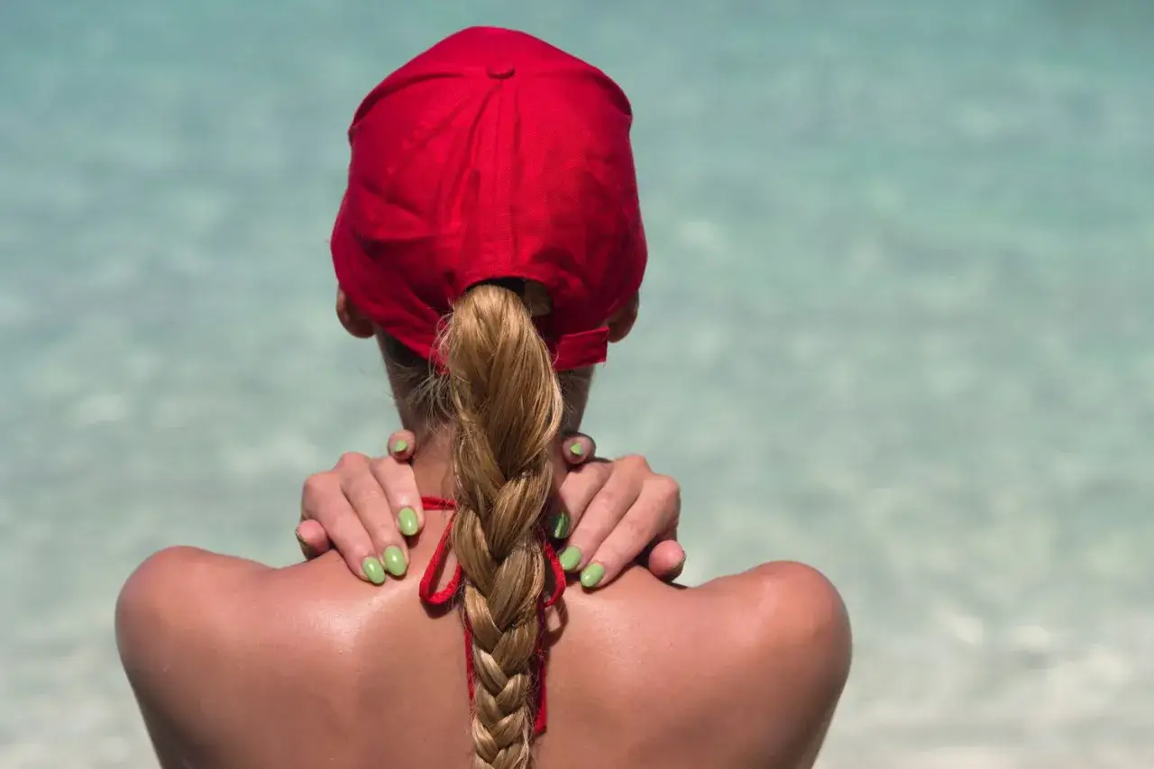 Frau mit geflochtenem Haar tr&auml;gt eine rote Cap richtig, die Sonne scheint auf ihre Schultern.