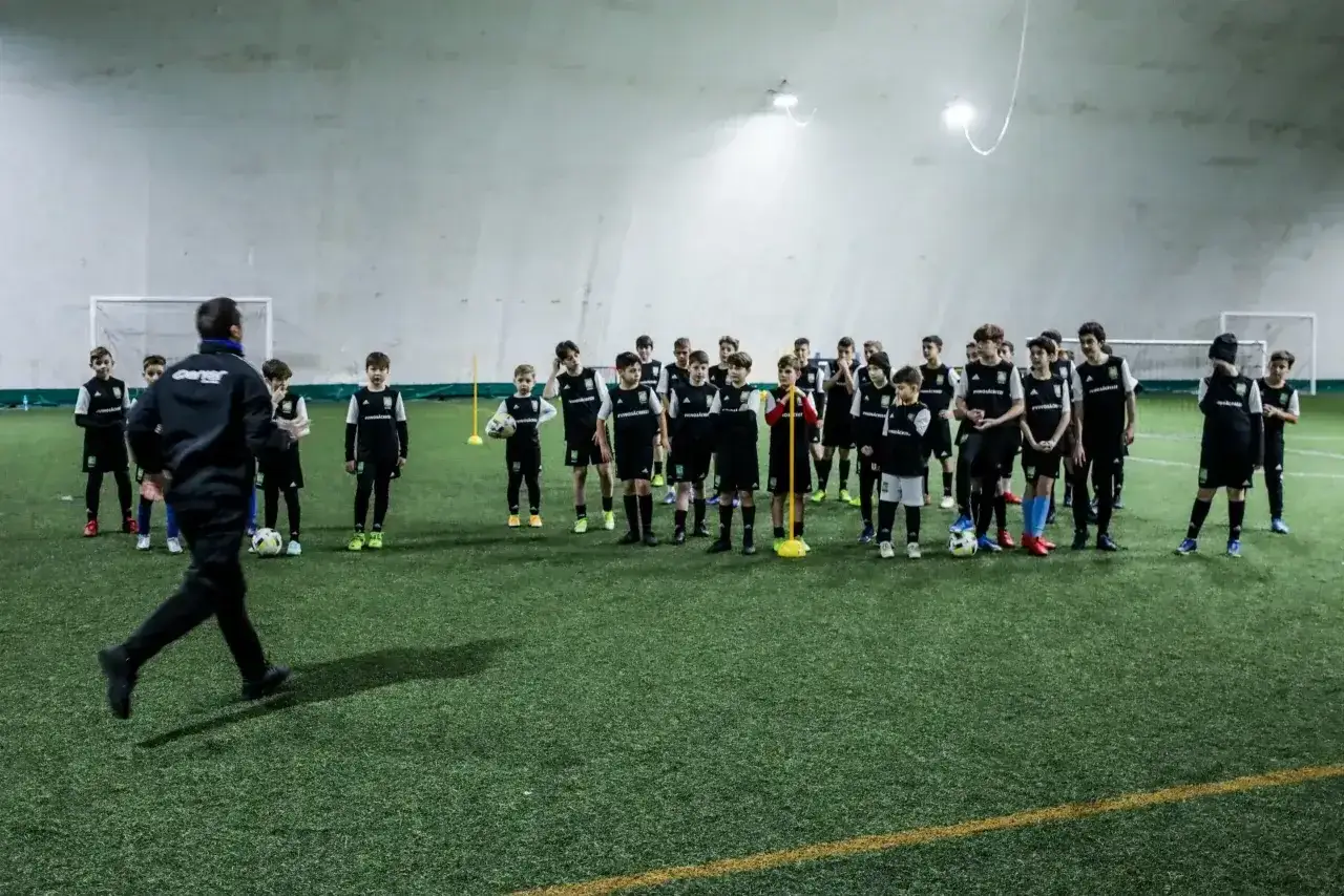 Trener prowadzi trening piłkarski dla młodych zawodników, stosując metody Coerver Coaching.