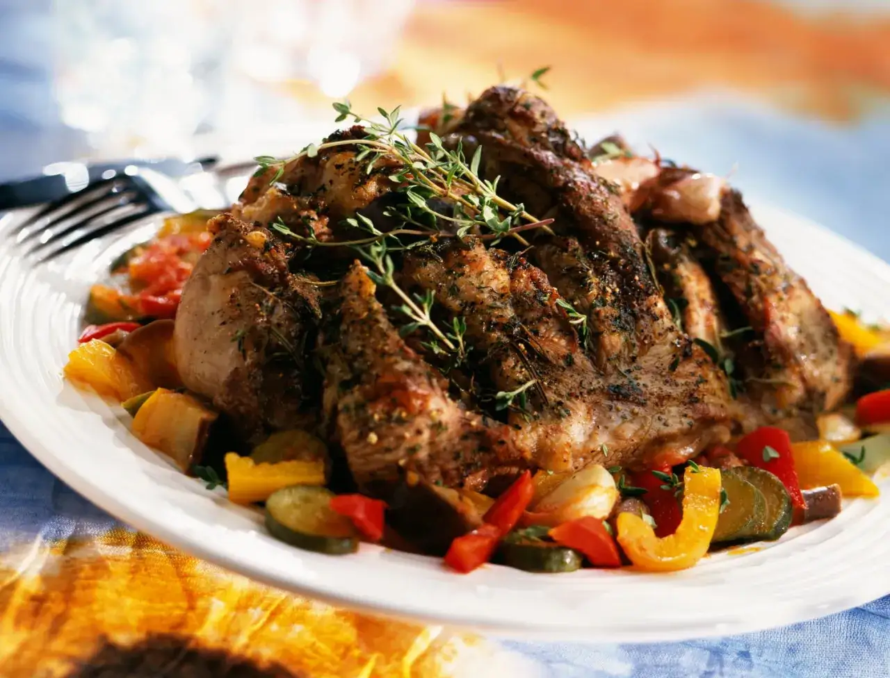 Selle d'agneau rôtie, garnie de thym frais, servie avec des légumes colorés poêlés. Un plat savoureux et appétissant.