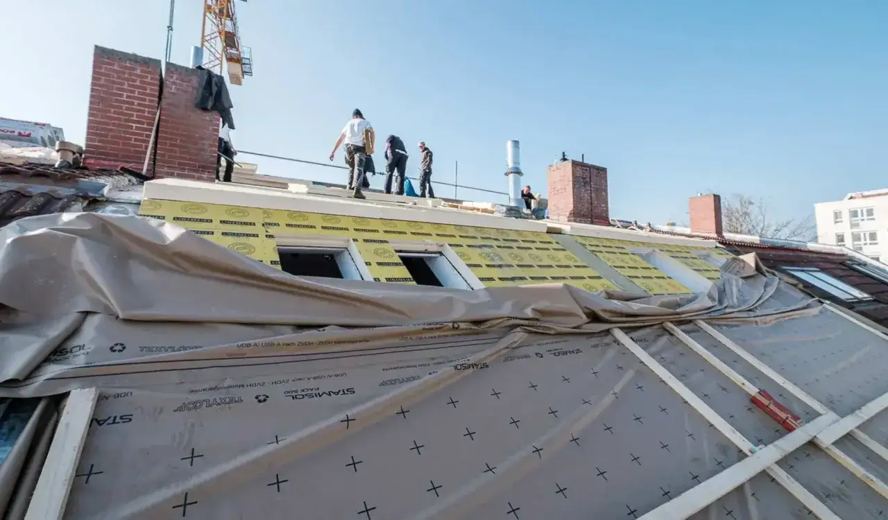 Arbeiter erneuern ein Dach. Neue D&auml;mmung und Folie werden angebracht, ein Kran steht bereit.