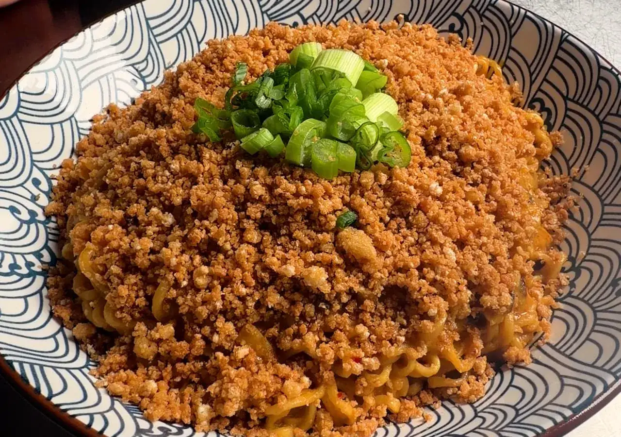 Miseczka pełna tantanmen, z makaronem w sosie, posypana chrupiącą mieloną wieprzowiną i zieloną cebulką.