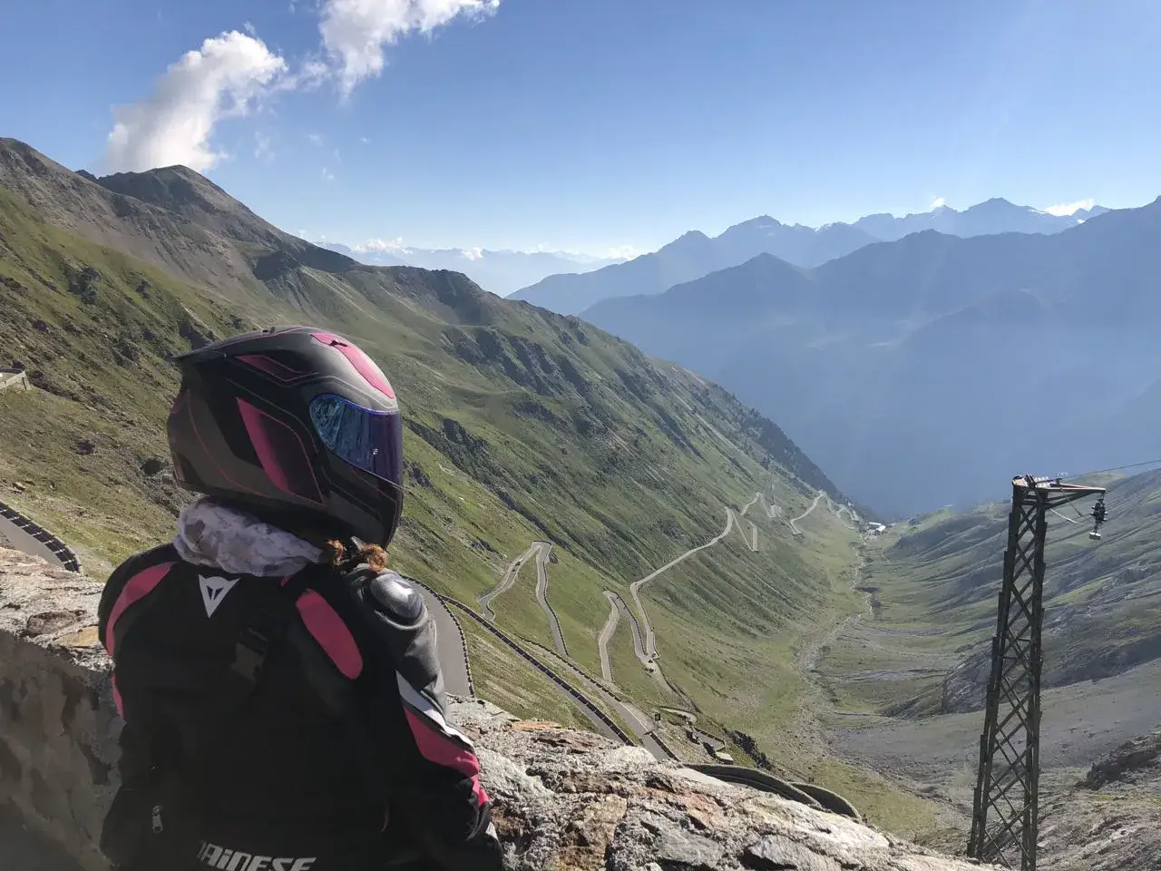 Motociclista ammira il panorama mozzafiato del passo dello Stelvio, un classico motogiro Lombardia. Curve a tornante si snodano tra le montagne verdi.