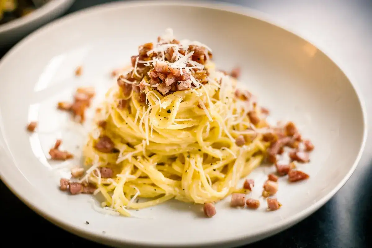 Pyszne spaghetti carbonara, przygotowane według oryginalnego przepisu ze śmietaną, posypane startym parmezanem i chrupiącym boczkiem.
