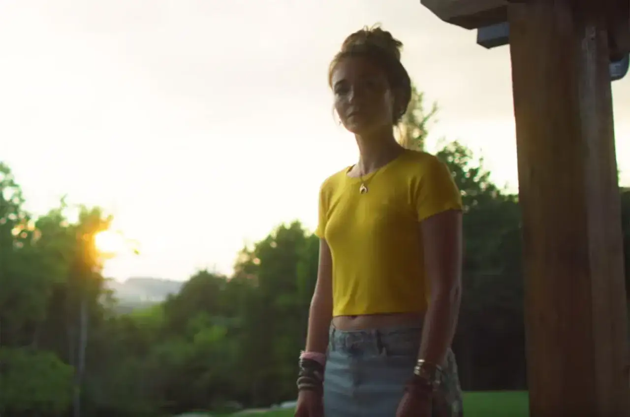 Lauren Daigle steht im Abendlicht vor einer Baumkulisse. Sie tr&auml;gt ein gelbes Crop-Top und Jeans.