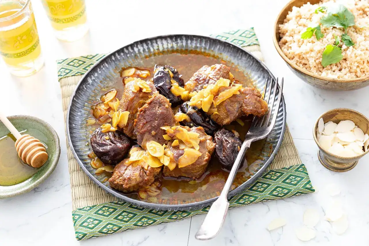 Un plat savoureux de tajine aux pruneaux, garni d'amandes effilées, servi avec du couscous et du miel.