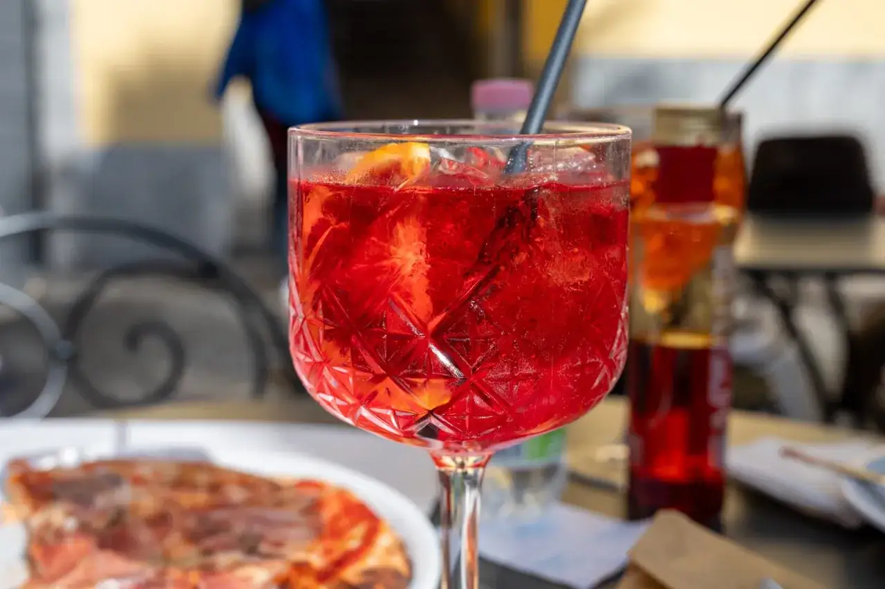 Czerwony drink z lodem i plasterkiem pomarańczy, idealny na aperitivo. Pyszne jedzenie i napoje w Mediolanie czekają!