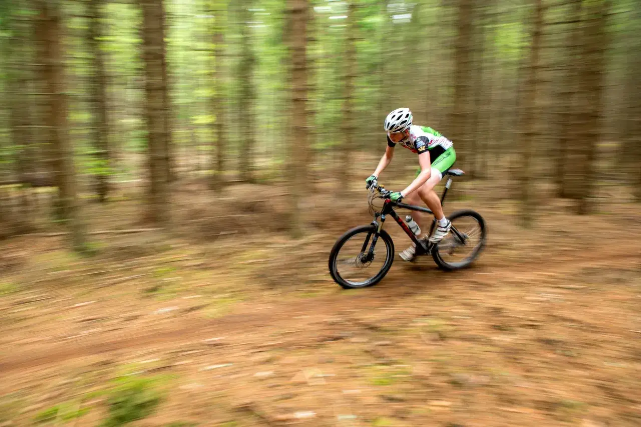 En person cyklar mtb genom en skog med suddiga träd i bakgrunden.