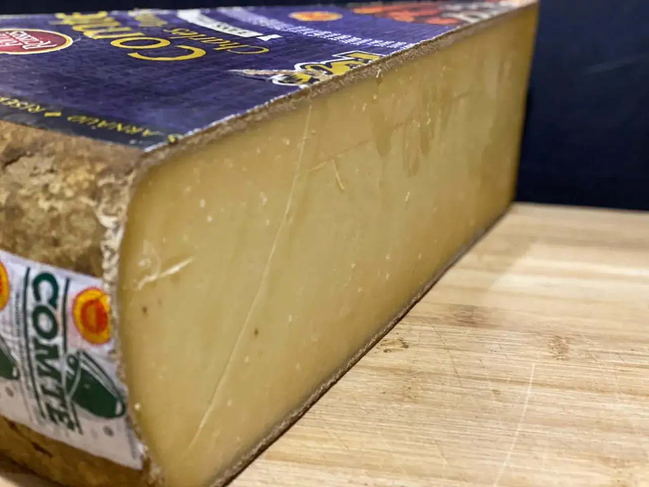 Un morceau de Comt&eacute; affin&eacute;, r&eacute;v&eacute;lant de d&eacute;licats cristaux dans le comt&eacute;, sur une planche en bois.
