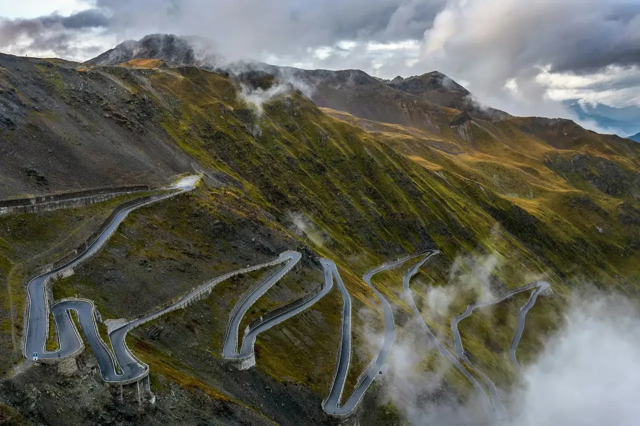 Strade da moto tortuose si snodano su un pendio montuoso, avvolte da nuvole e nebbia. Un paesaggio mozzafiato per avventure su due ruote.