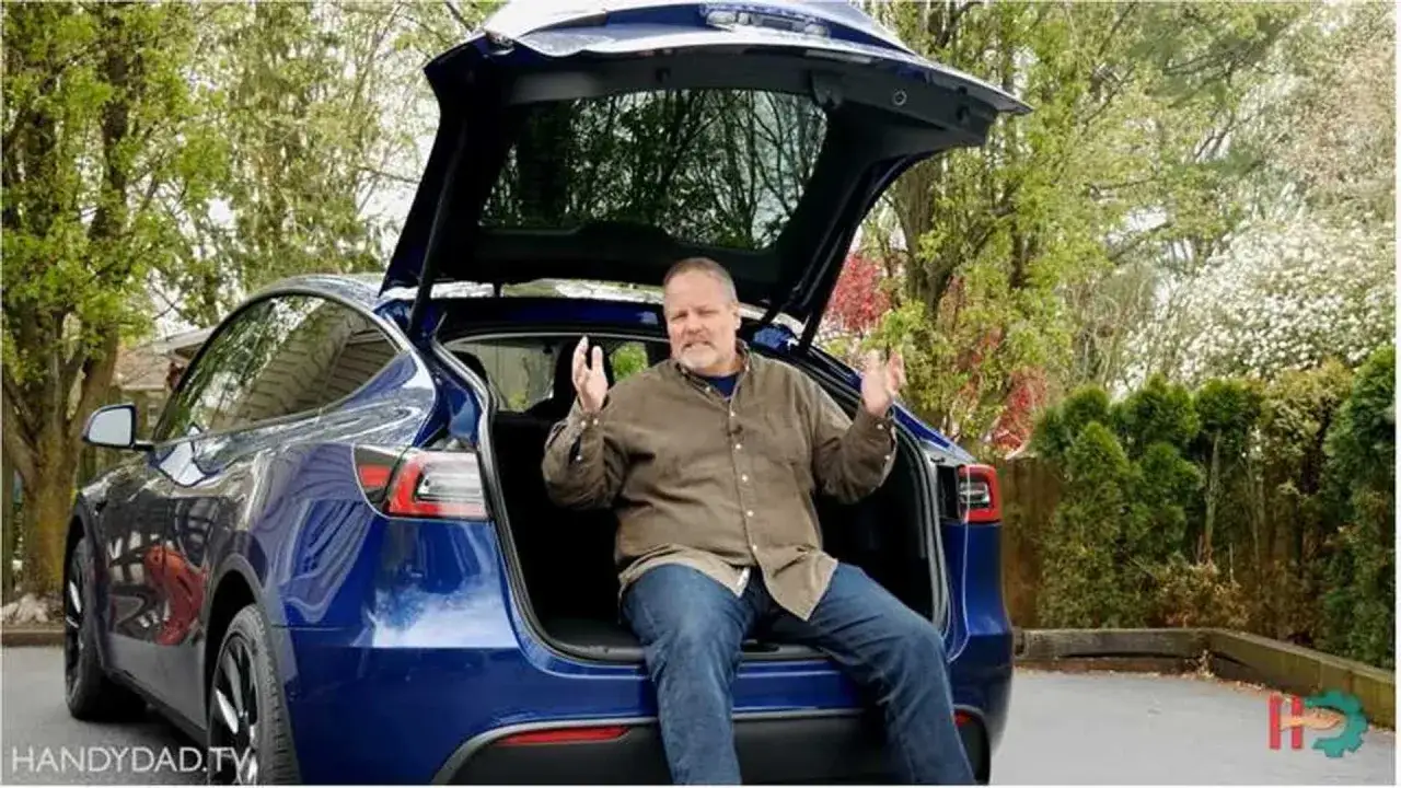 Un homme est assis dans le coffre ouvert d'une Tesla Model Y bleue, expliquant ses fonctionnalit&eacute;s.