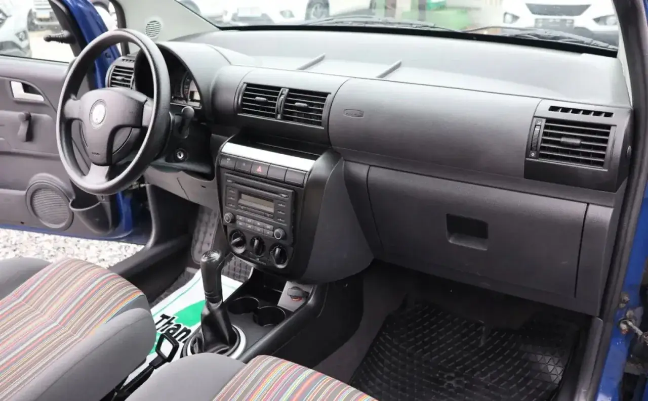 Wnętrze Volkswagena Fox 2006: kierownica, deska rozdzielcza z radiem i nawiewami, kolorowe siedzenia.