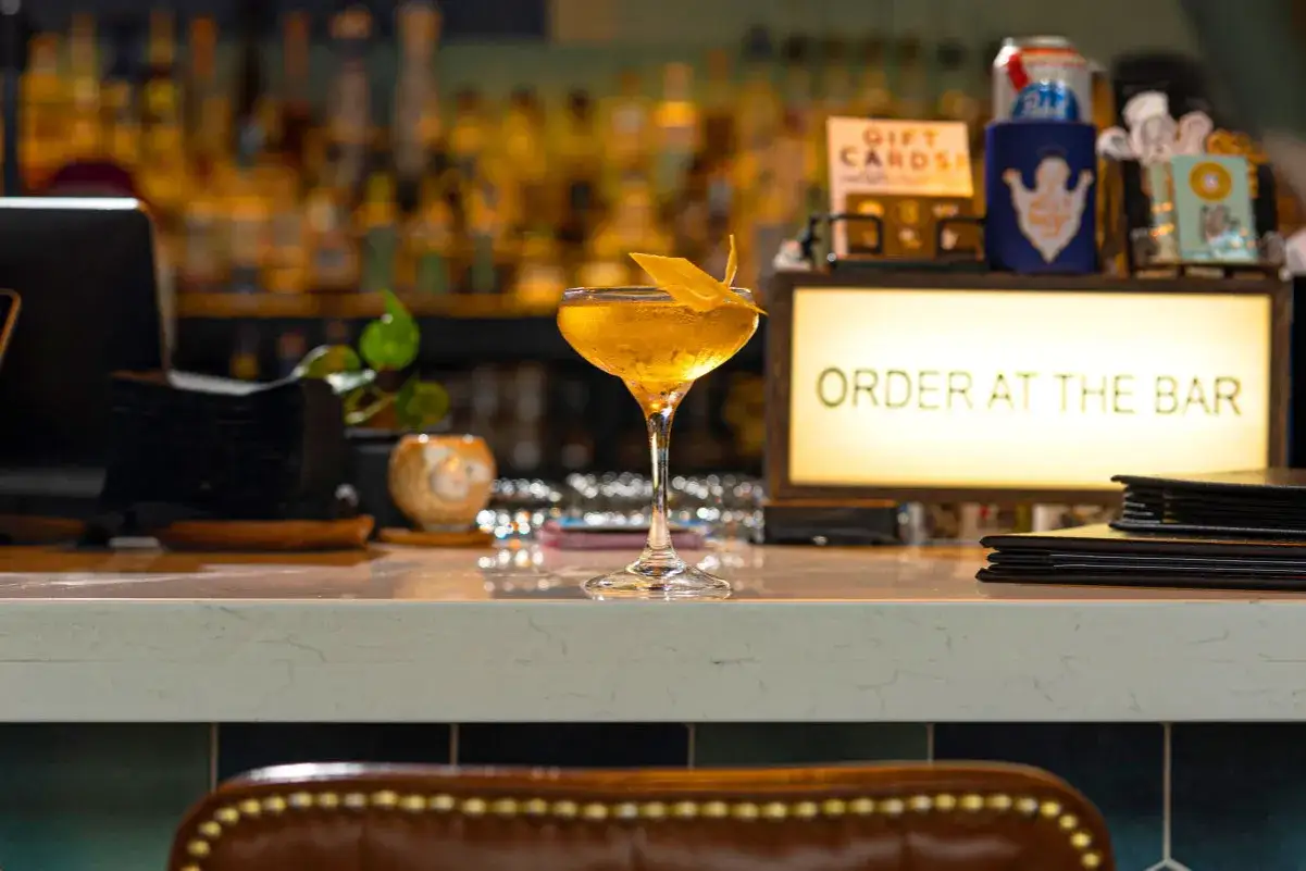 Elegancki drink z mezcalem czy z tequilą, ozdobiony skórką cytrusową, czeka na zamówienie przy barze.