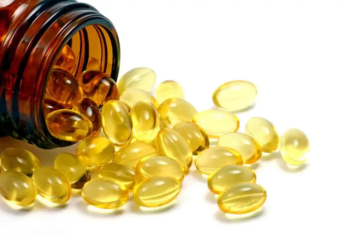 G&eacute;lules dor&eacute;es renvers&eacute;es d'un flacon ambr&eacute;, &eacute;voquant la vitamine D pour des cheveux &eacute;clatants de sant&eacute;.