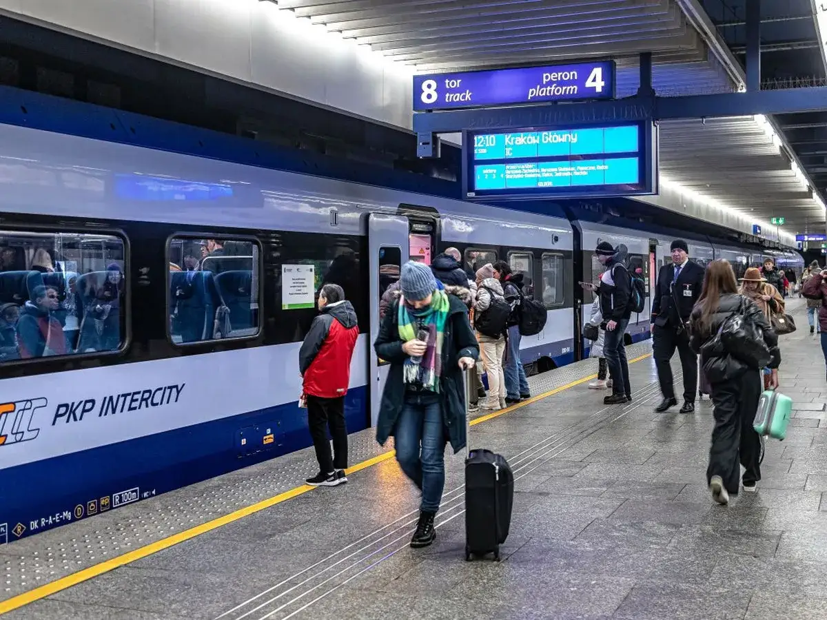 Na dworcu PKP Intercity ludzie z bagażami czekają na pociąg. Czy można kupić bilet w pociągu Intercity? Informacja na tablicy wskazuje odjazd do Krakowa Głównego.