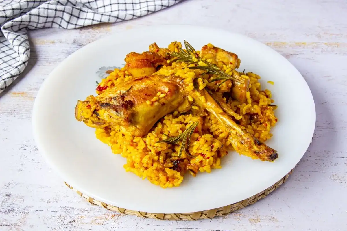 Un plato de arroz con conejo, cocinado a la perfecci&oacute;n, con trozos dorados de carne y adornado con romero fresco.