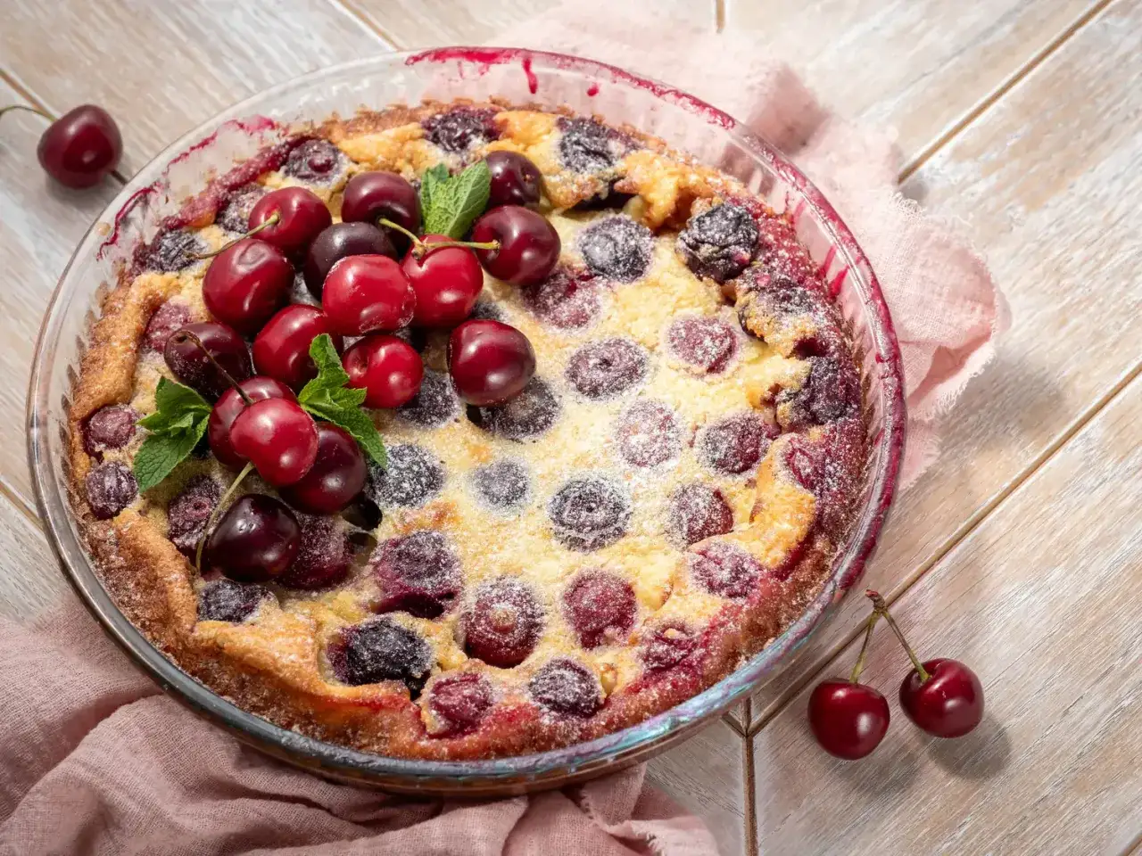 Clafoutis aux cerises, une recette de Laurent Mariotte, doré et saupoudré de sucre glace, garni de cerises fraîches et de menthe.