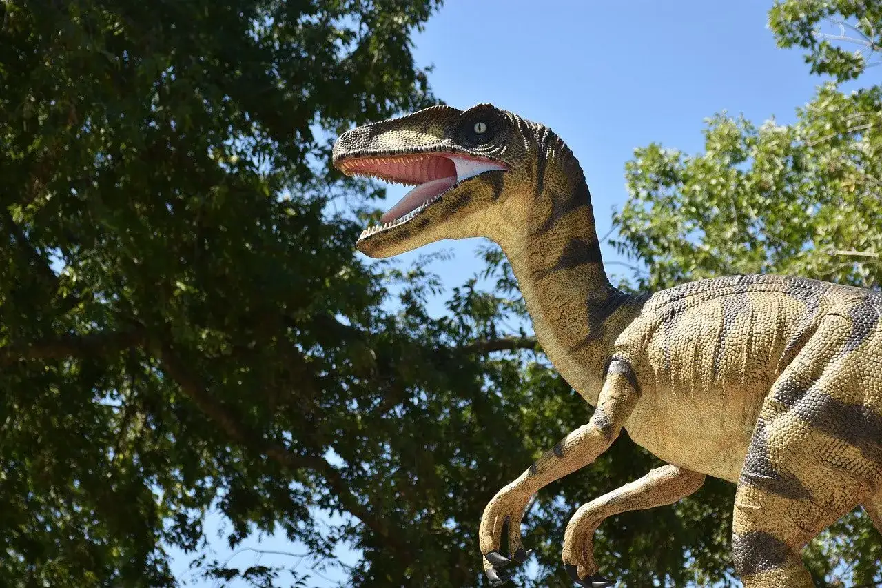 Model dinozaura z otwartym pyskiem, jakby wyłaniał się z drzew. Idealna atrakcja dla odwiedzających muzeum dinozaurów w Krakowie.