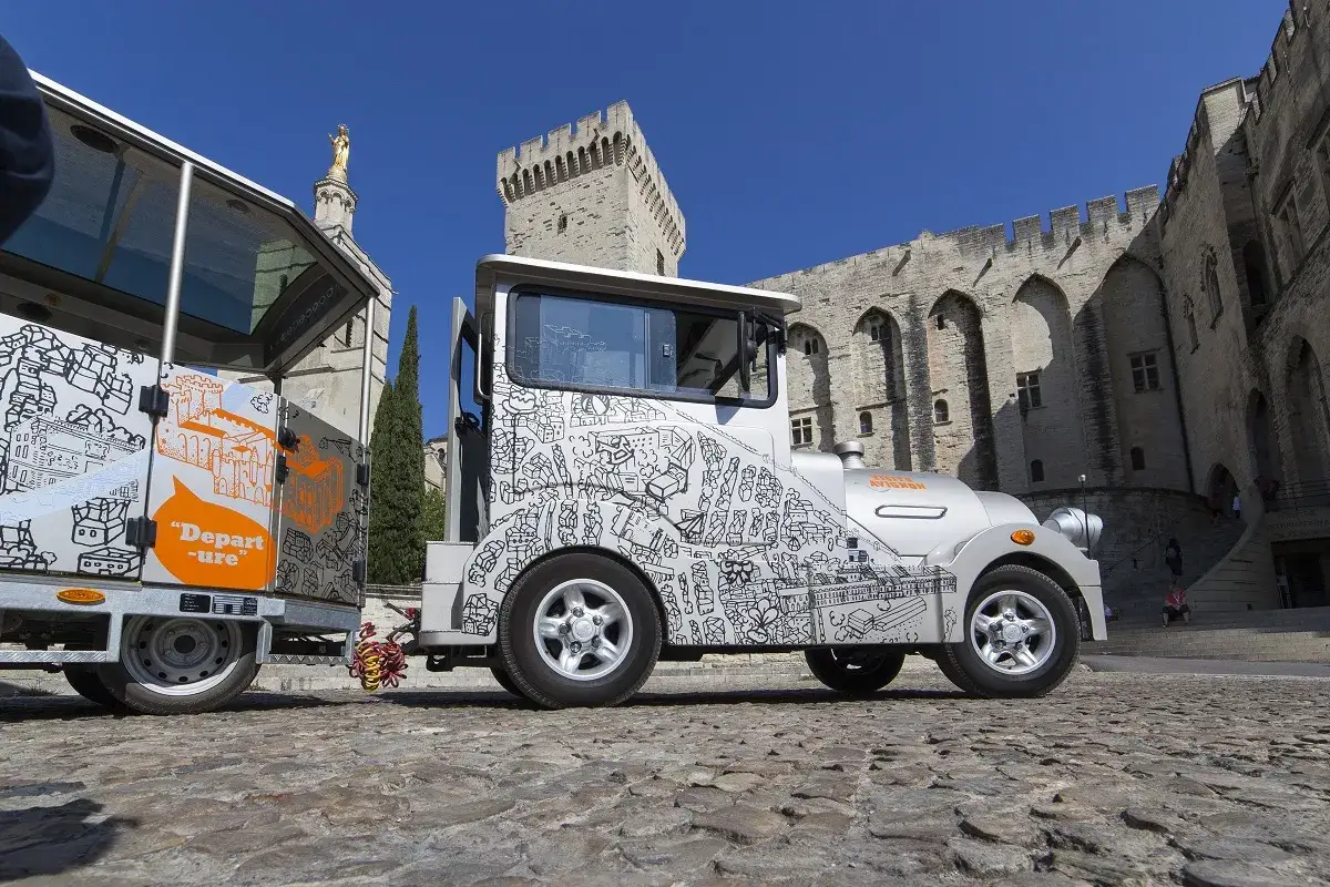 Le petit train touristique d'Avignon, d&eacute;cor&eacute; de dessins de la ville, attend les visiteurs devant le Palais des Papes.