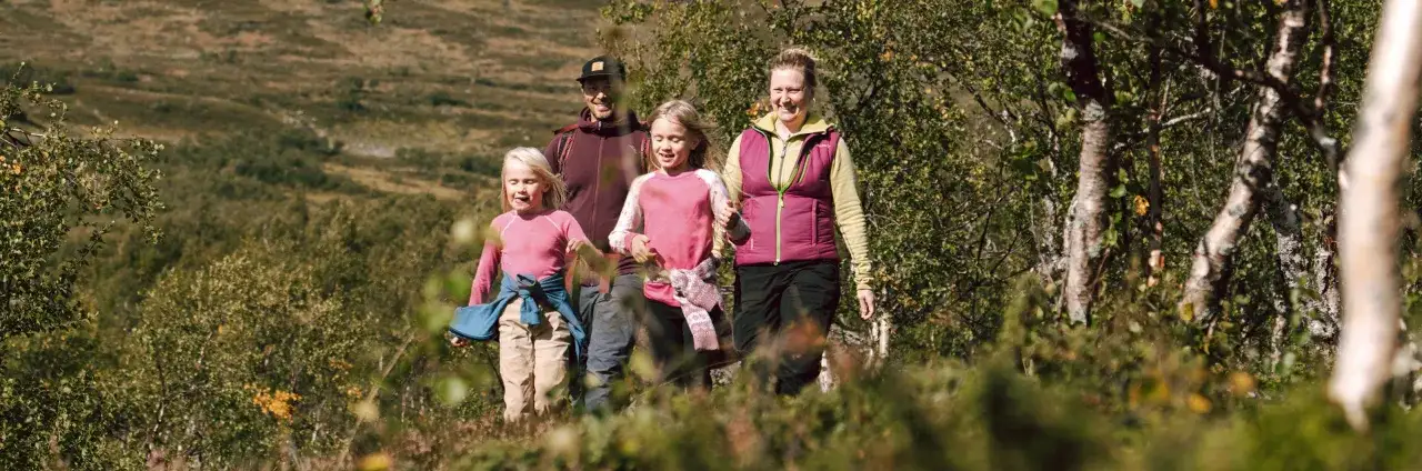 En familj njuter av en h&auml;rlig dag att vandra med barn i fj&auml;llen. Solen skiner och de skrattar sig fram genom den gr&ouml;na naturen.