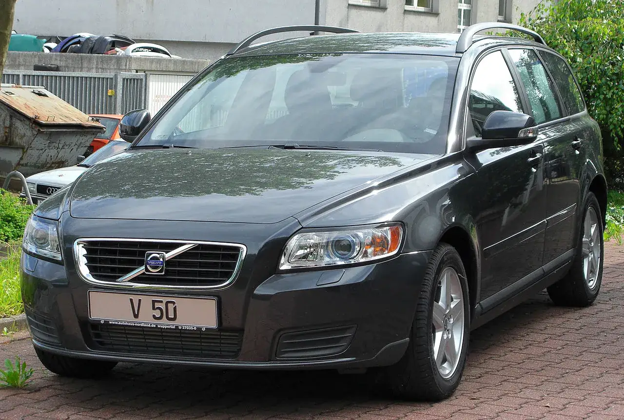 Ciemnoszary Volvo V50 2.0D na tle budynku i śmietników.
