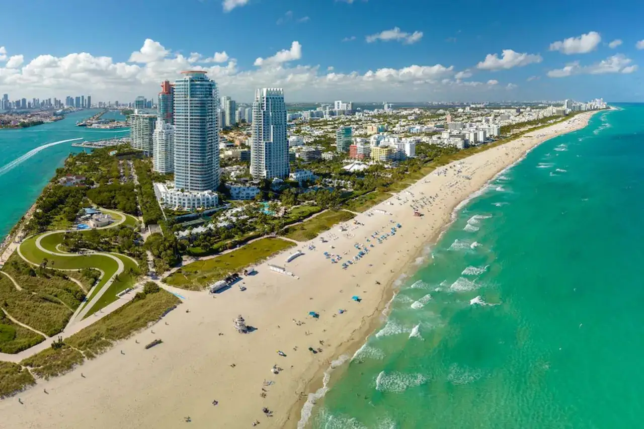 Piękna miami pogoda. Słoneczny dzień na plaży z turkusową wodą, białym piaskiem i wysokimi budynkami w tle.