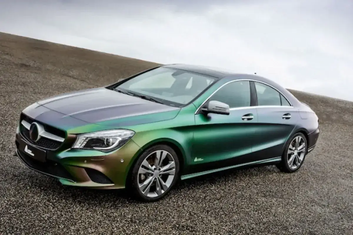 Mercedes CLA z folią Avery Dennison w kolorze zielono-fioletowym, stojący na żwirowym podłożu.