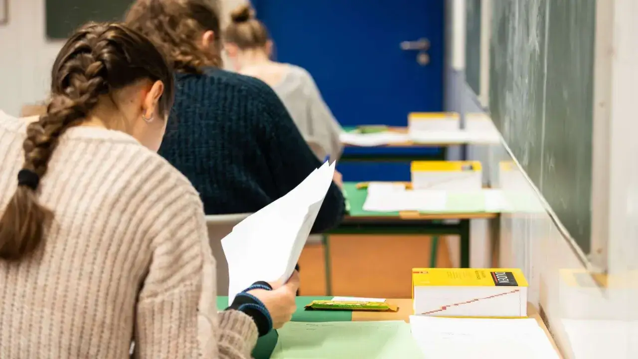 Sch&uuml;lerin mit Zopf h&auml;lt Pr&uuml;fungsbogen, ein Duden liegt bereit. Hoffentlich wird sie nicht beim Spicken erwischt.