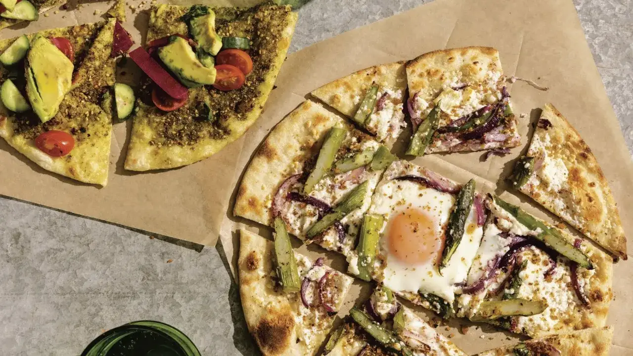 Två liba pizzor, en med grönsaker och avokado, den andra med ägg, sparris och lök.