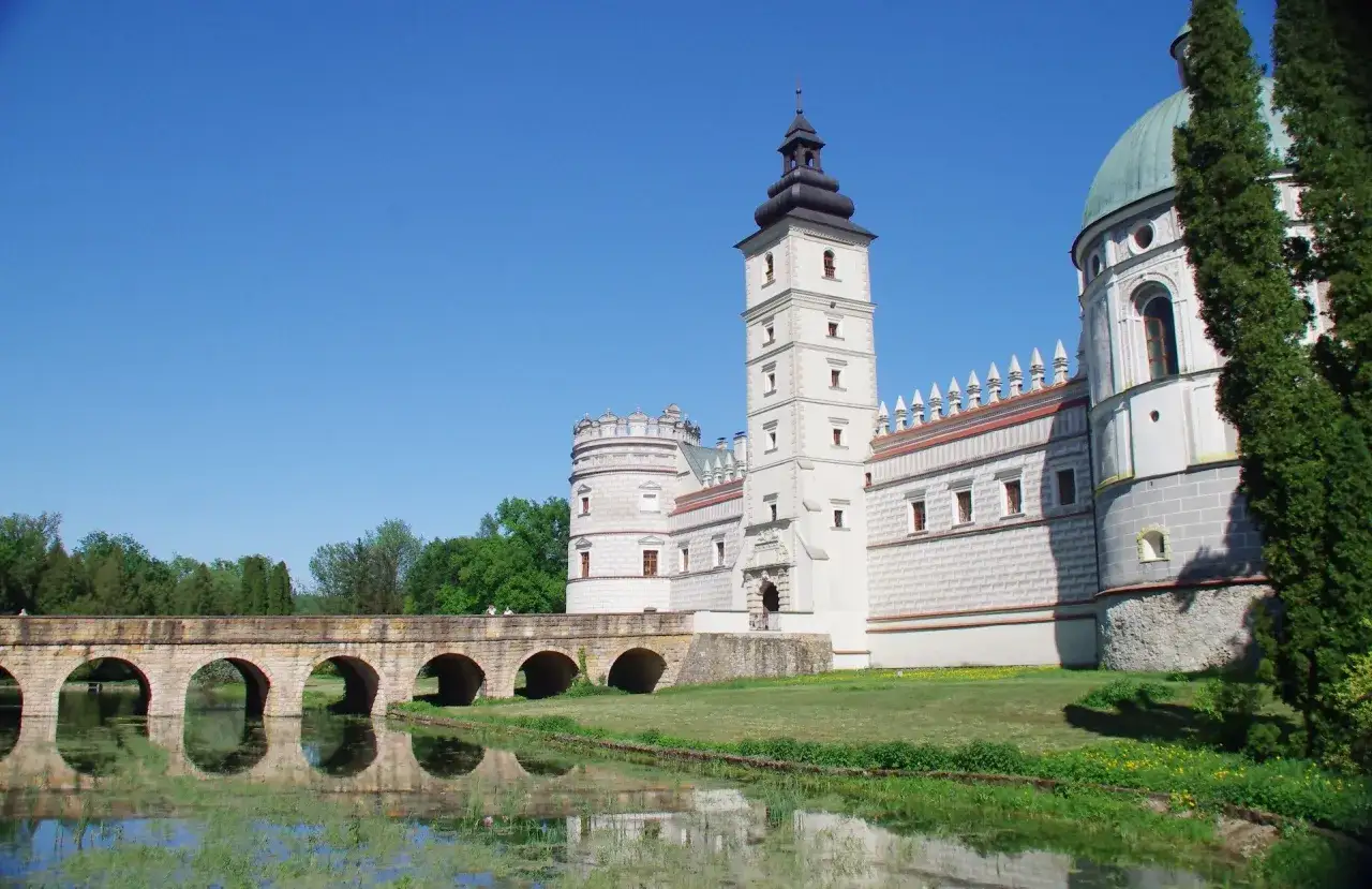 Krasiczyn zamek zwiedzanie: malowniczy widok na zamek z mostem nad fosą, odbijający się w wodzie.