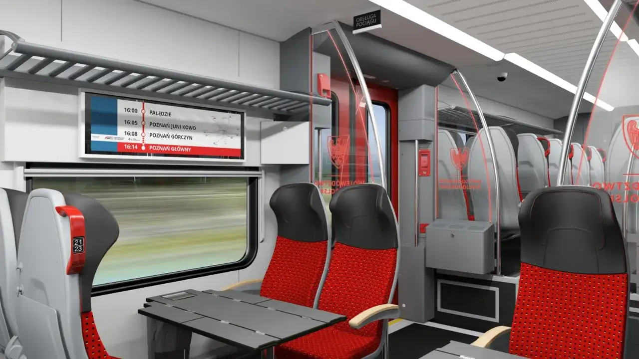 Wnętrze pociągu Stadler FLIRT z czerwono-szarymi siedzeniami. Na ekranie wyświetlane są czasy odjazdów z Poznania.