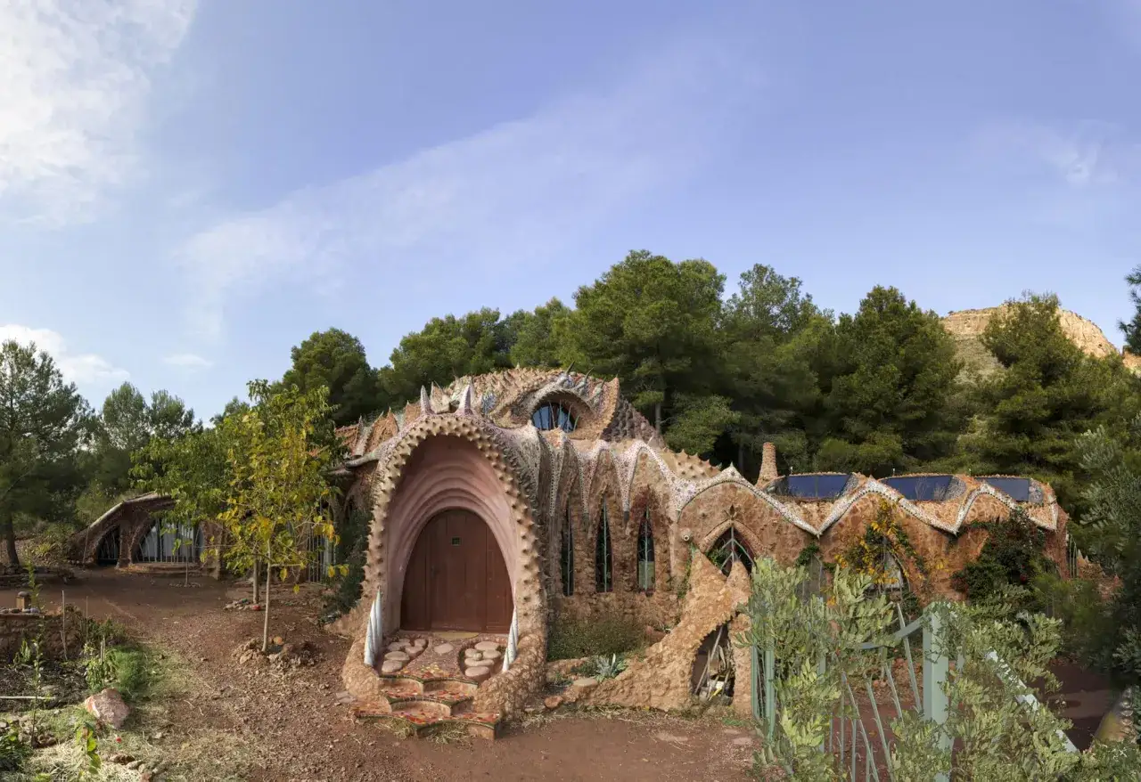 La casa del dragón de Gilet, una maravilla arquitectónica con tejado escamoso y entrada curva, se alza entre pinos.
