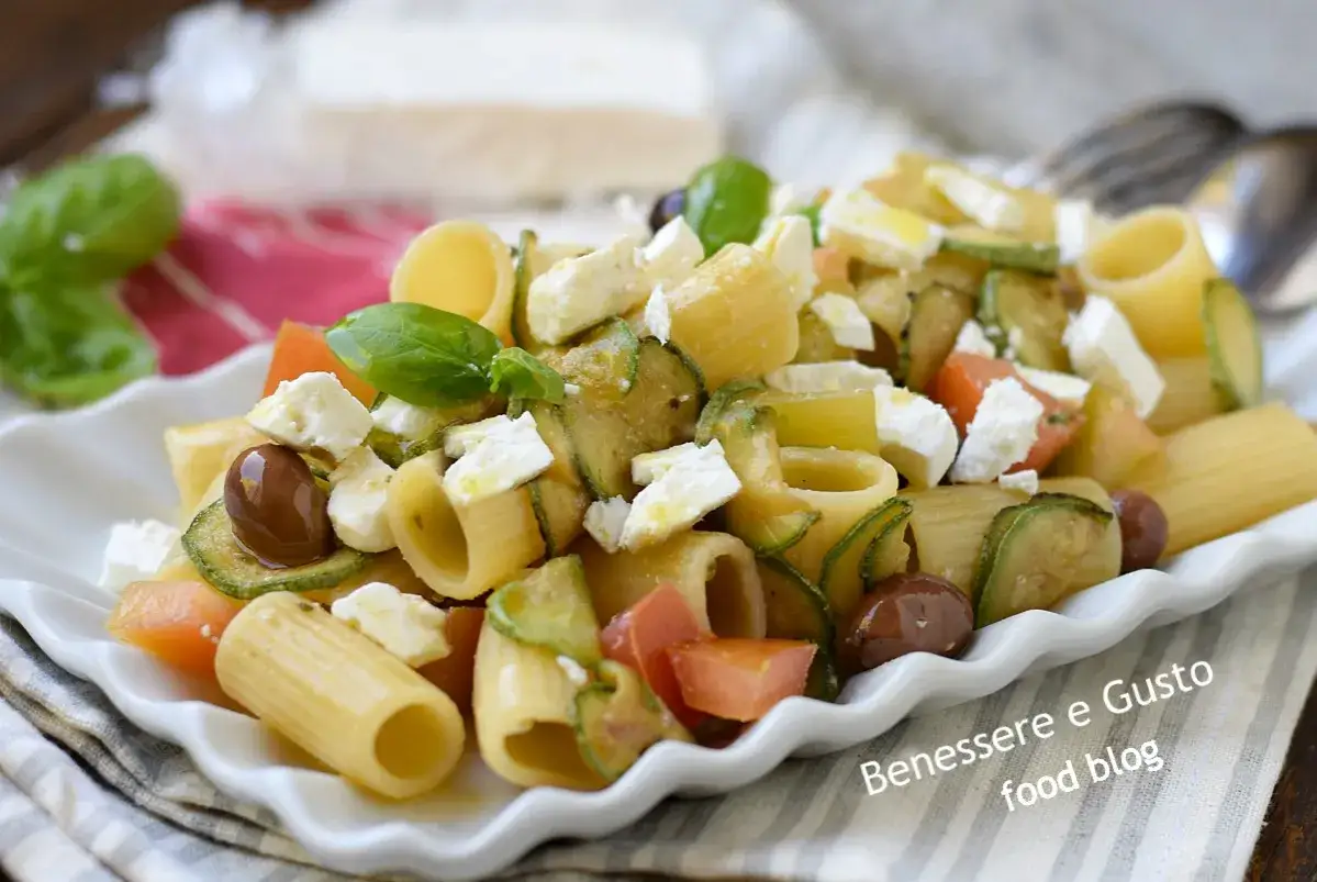 Pasta fredda con feta, zucchine, pomodorini e olive nere. Un piatto estivo fresco e saporito, perfetto per un pranzo leggero.