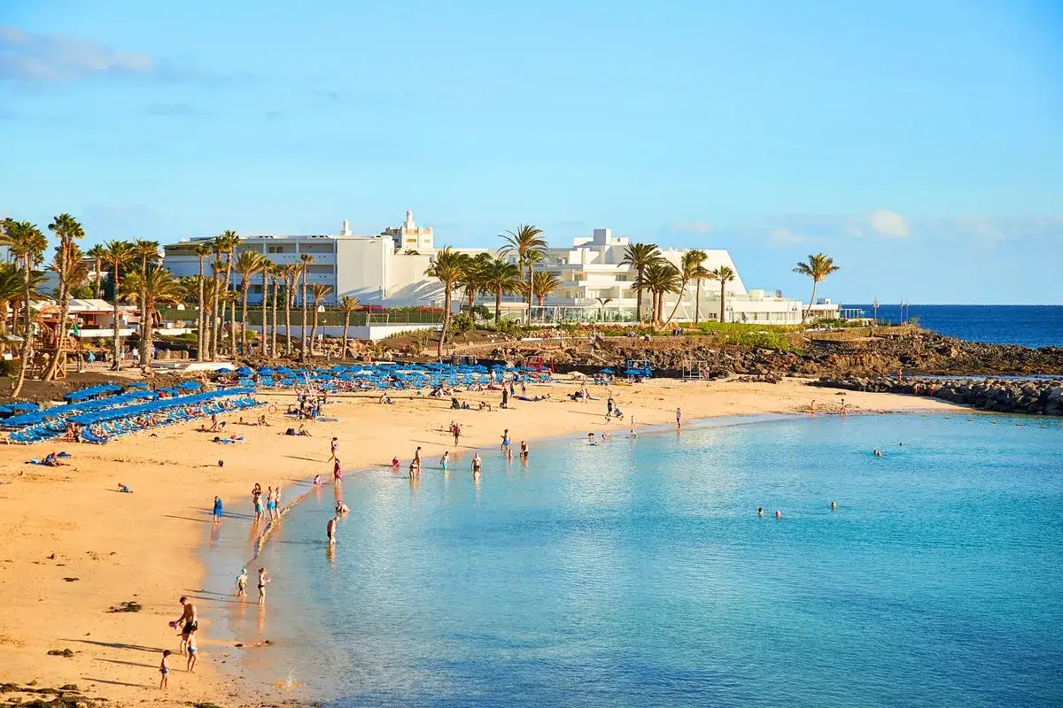 Sonniger Strand mit Palmen und Menschen im Wasser. Selbst im Spanien Winter ist die Temperatur angenehm f&uuml;r einen Strandtag.