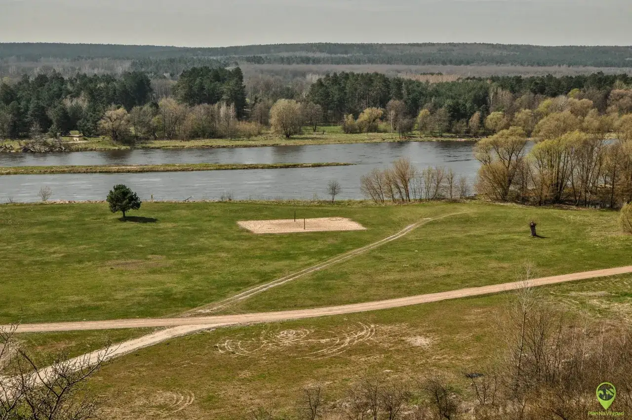 Łąka z boiskiem do siatkówki plażowej i rzeką w tle. W oddali las. Mielnik atrakcje przyrodnicze.