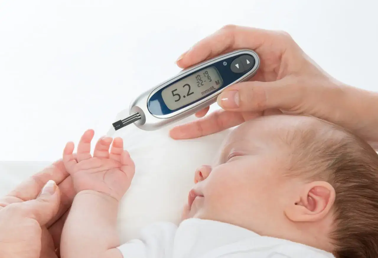 Mano che tiene glucometro vicino al piedino di un neonato, monitorando i livelli di glucosio per il diabete neonatale.