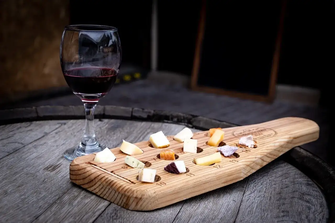 Un bicchiere di vino rosso accanto a un tagliere di legno con vari formaggi, perfetto per un abbinamento di vino per formaggi.